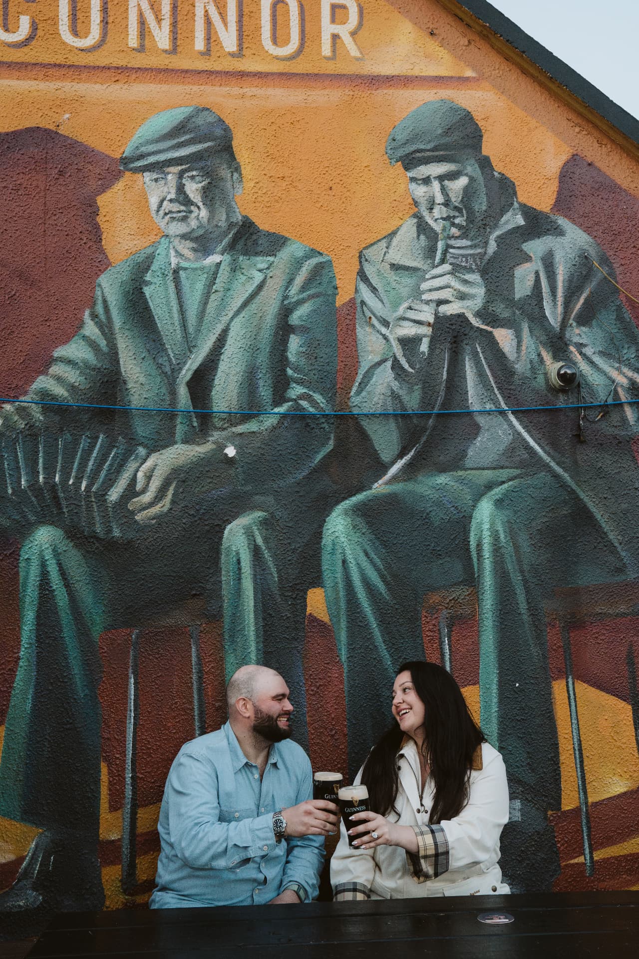 Jaime and Nolan laughing over a toast outside the pub