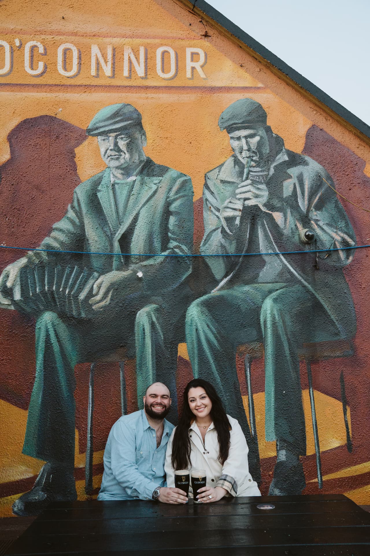 Jaime and Nolan with two pints under the O'Connor's mural