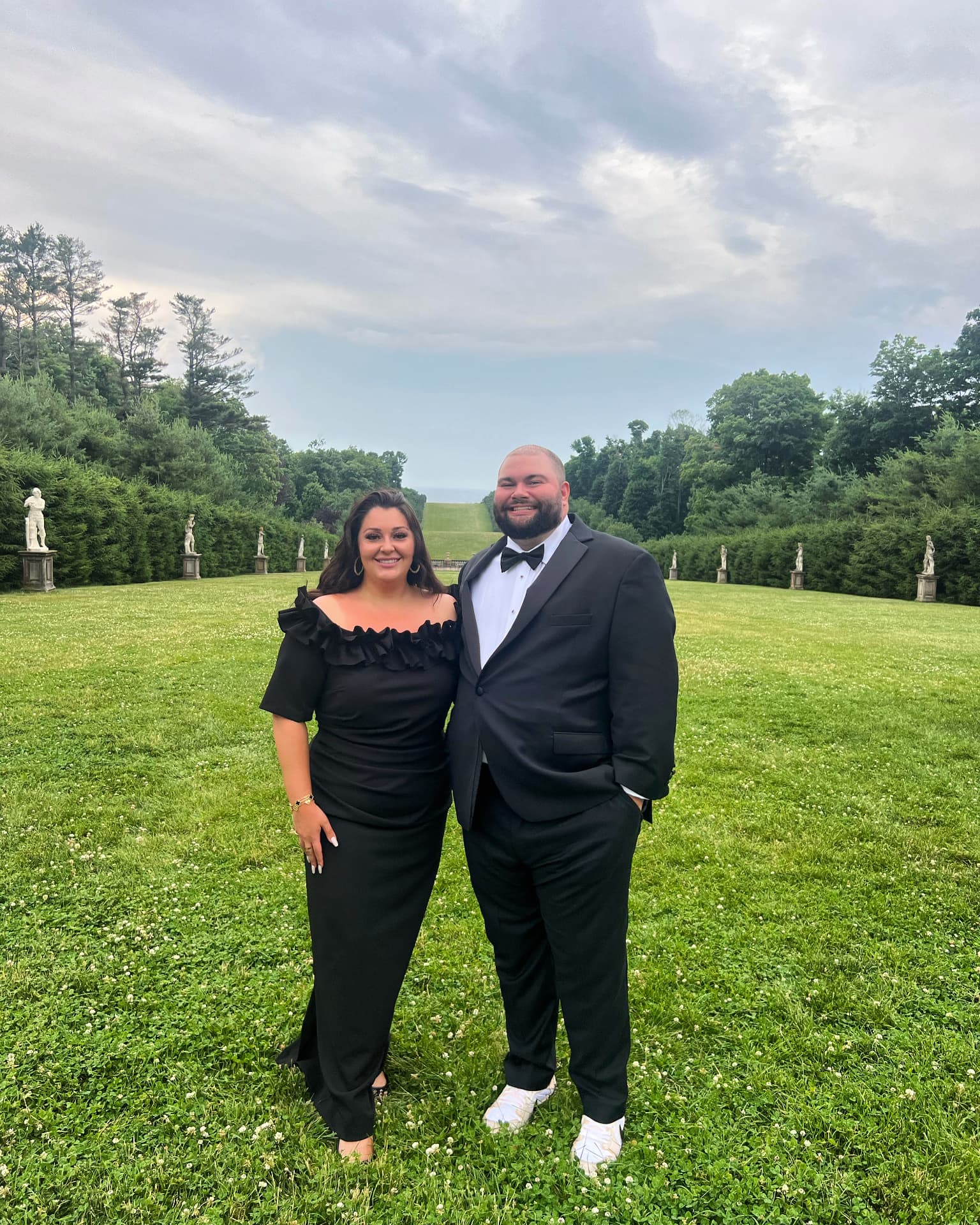 Jaime and Nolan in black tie on the lawn of a statue-lined estate garden